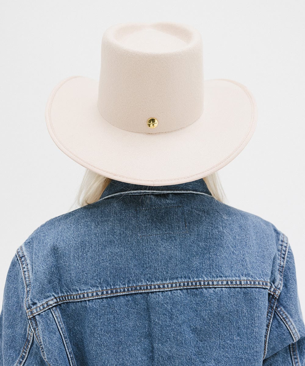 Person wearing a beige hat and denim jacket on a light gray background