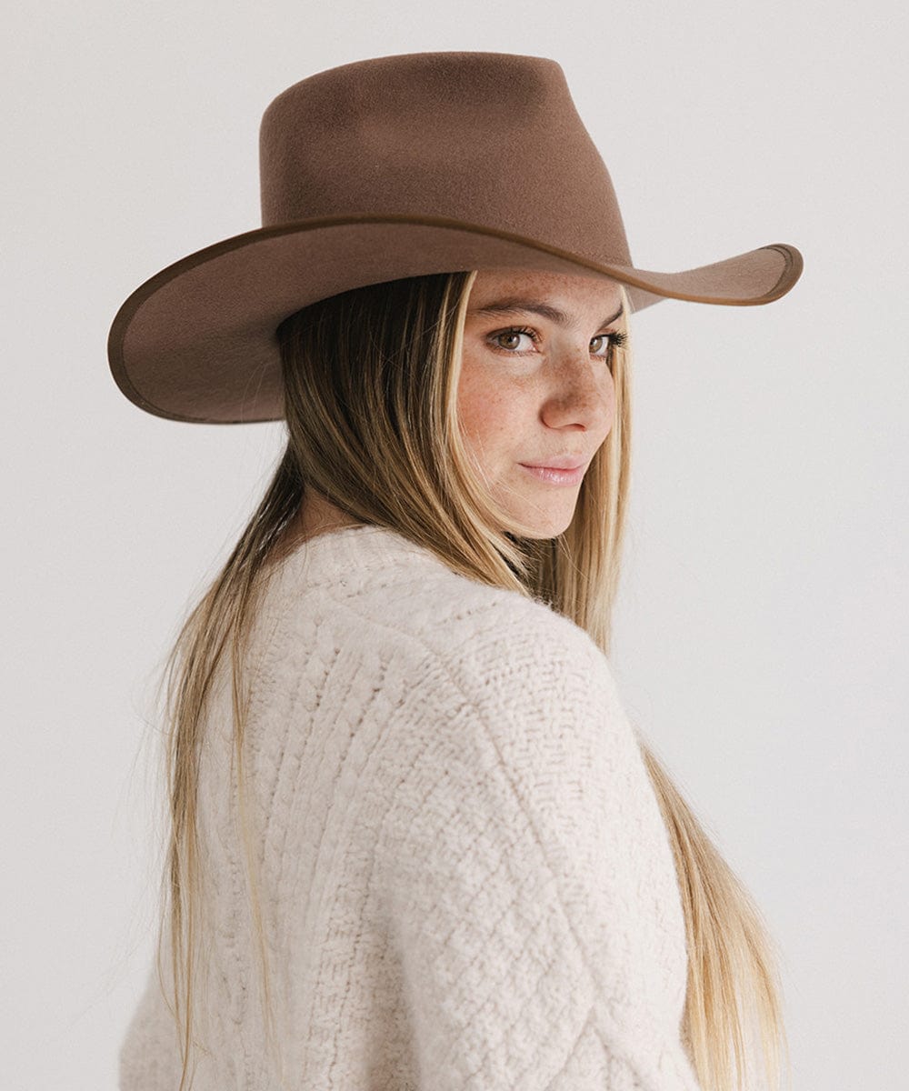 Woman wearing a brown hat and white sweater against a plain background