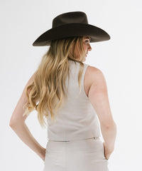Woman wearing a wide-brimmed black hat and white sleeveless top on a light gray background