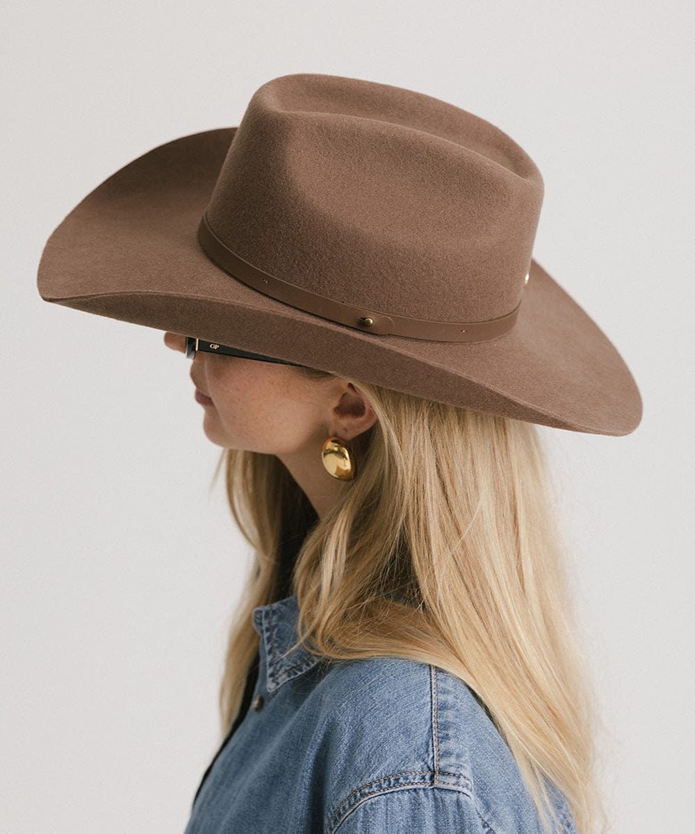 Person wearing a brown cowboy hat and denim jacket on a plain background