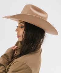 Woman wearing a beige cowboy hat and coat on a light gray background