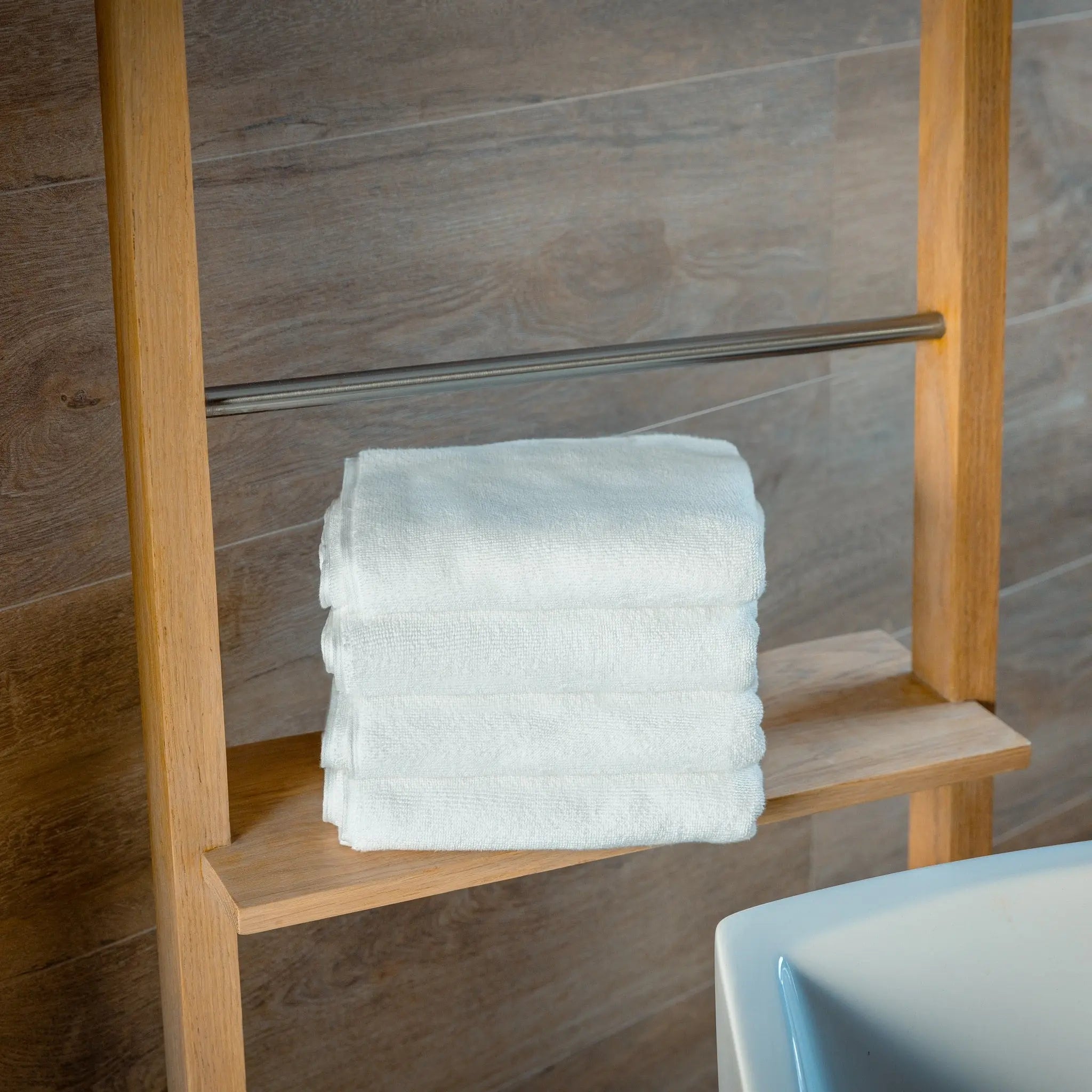 Stack of white towels on a wooden towel rack against a tiled wall.