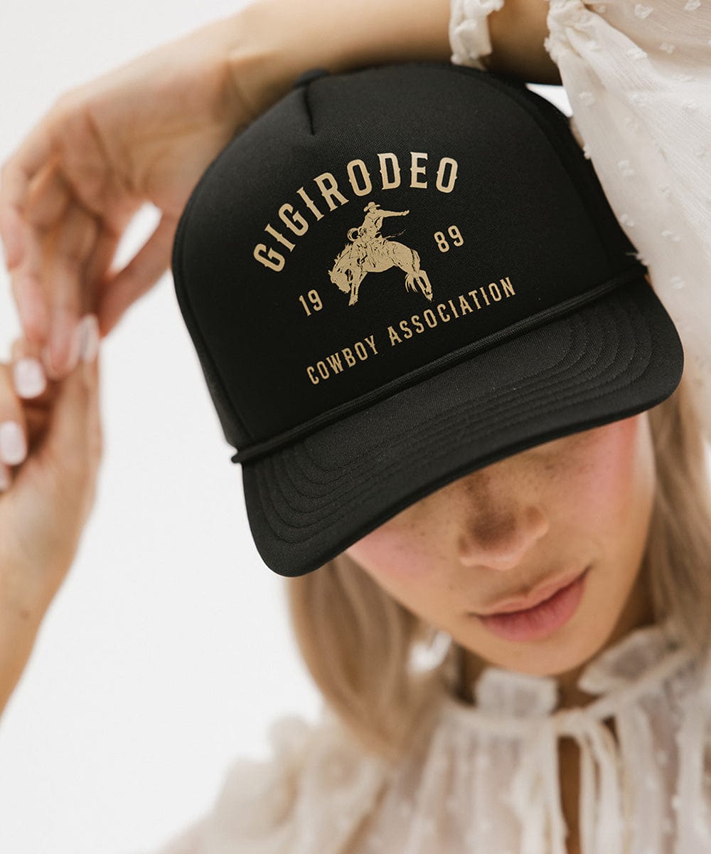 Black cap with gold text and logo held by a person wearing a white lace top.