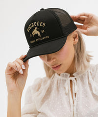 Person wearing a black cap with gold text and logo on a light background