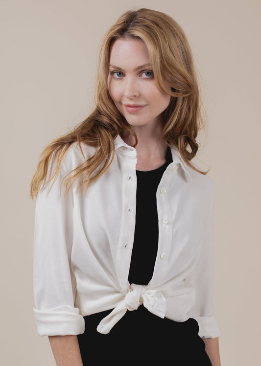 Woman wearing a white blouse with a black top underneath on a beige background