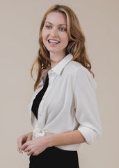 Woman wearing a white blouse over a black top against a beige background