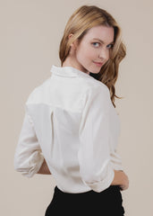 Woman wearing a white blouse with long sleeves against a beige background
