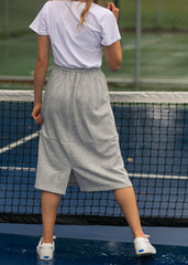 Person wearing a white shirt and gray wide-leg pants standing on a tennis court.