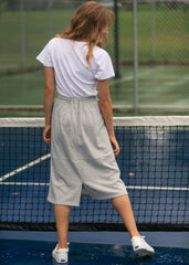 Person standing on a tennis court wearing a white t-shirt and gray pants.