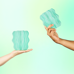 Two hands holding green wavy-patterned objects against a light green background