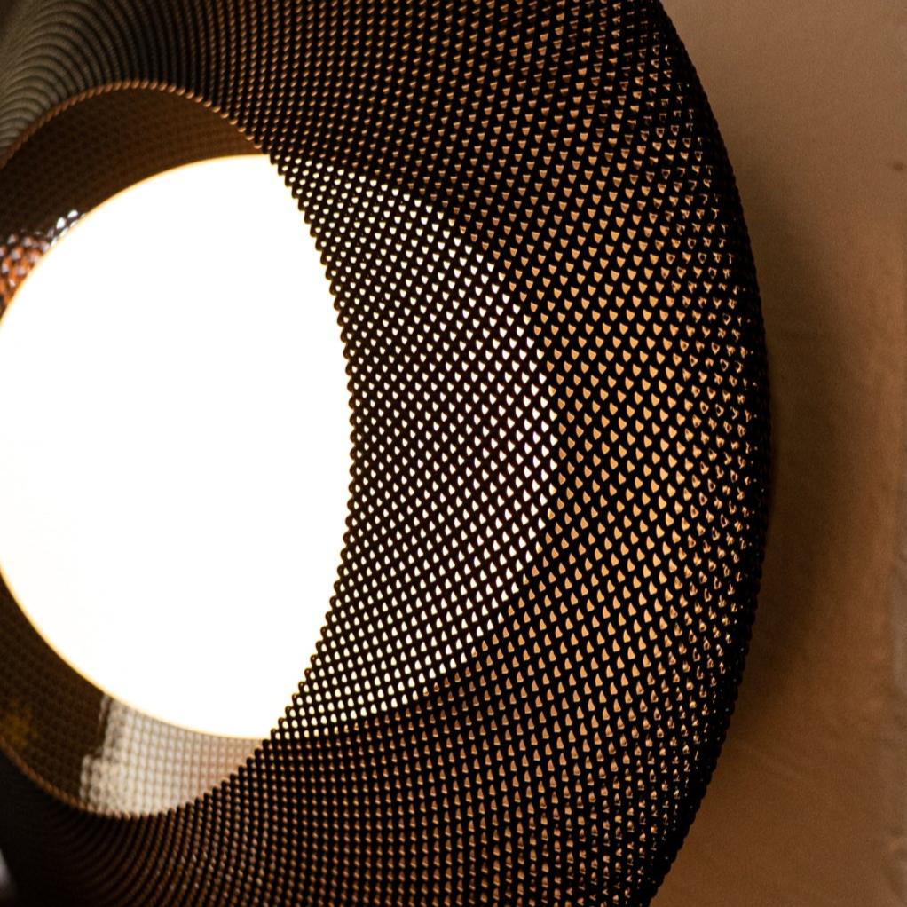 Close-up of a light fixture with a mesh cover on a beige wall.