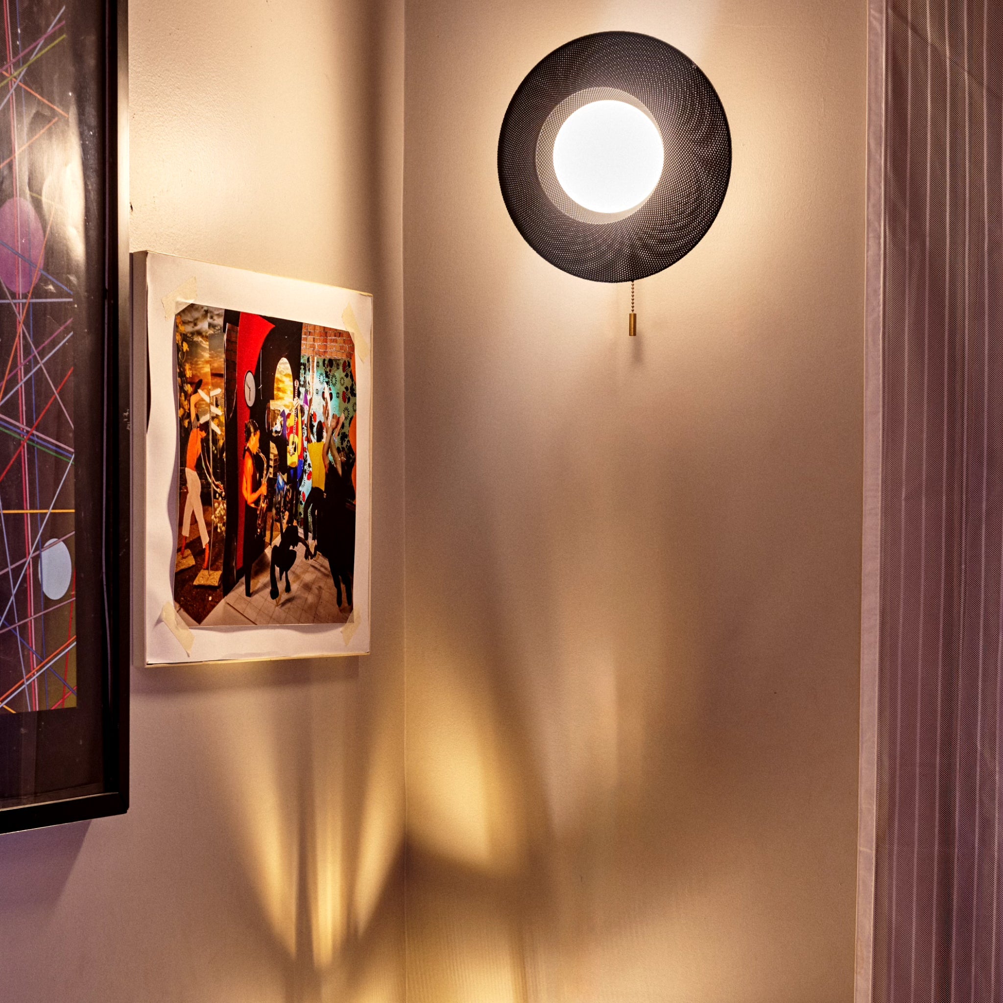 Wall-mounted light fixture casting a shadow on a wall with framed artwork.