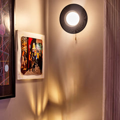 Wall-mounted light fixture casting a shadow on a wall with framed artwork.