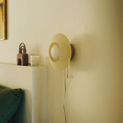 Round wall lamp on a beige wall with a shelf and decorative items in the background.