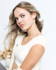 Woman with long blonde hair wearing a white dress against a light background