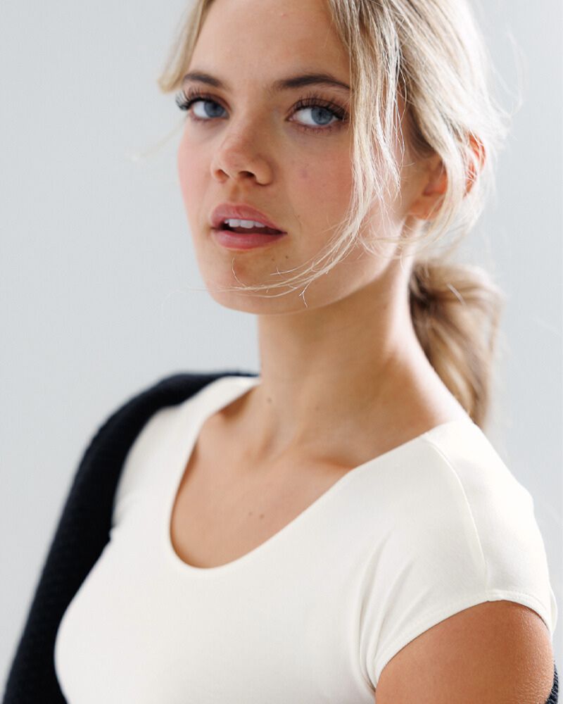 Woman with blonde hair wearing a white top against a light background