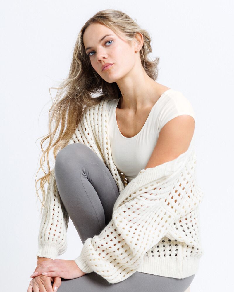 Woman wearing a white top and gray leggings with a white cardigan on a light background