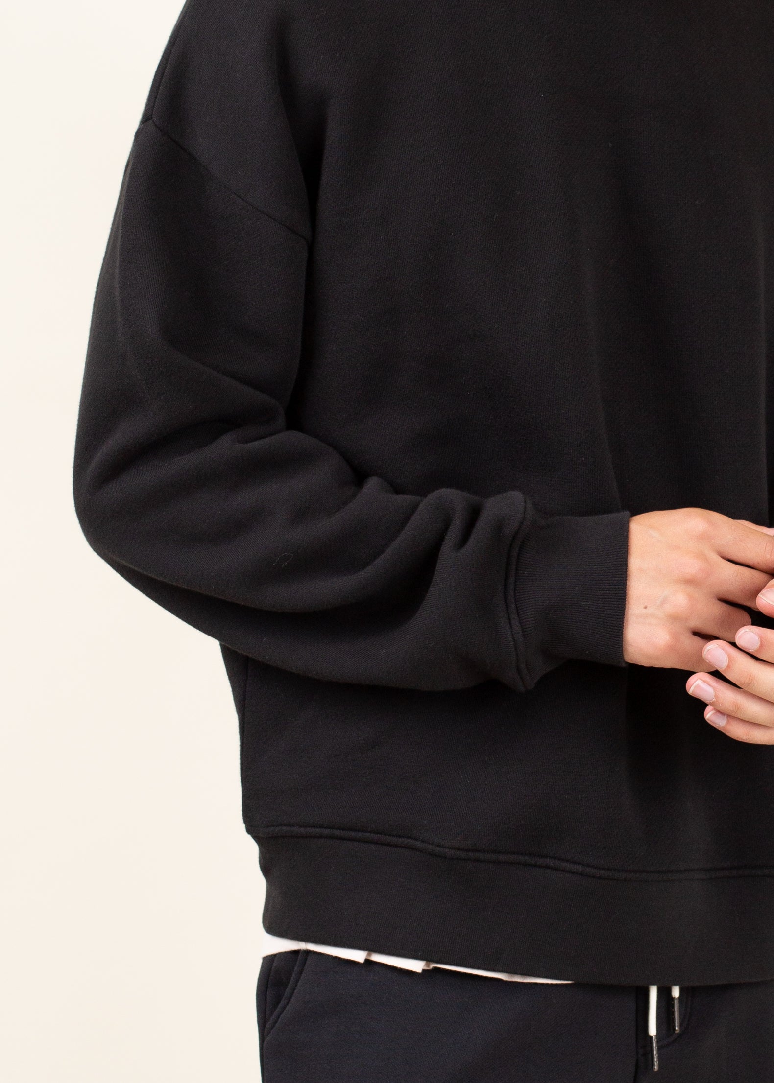 Black hoodie worn by a person on a light beige background
