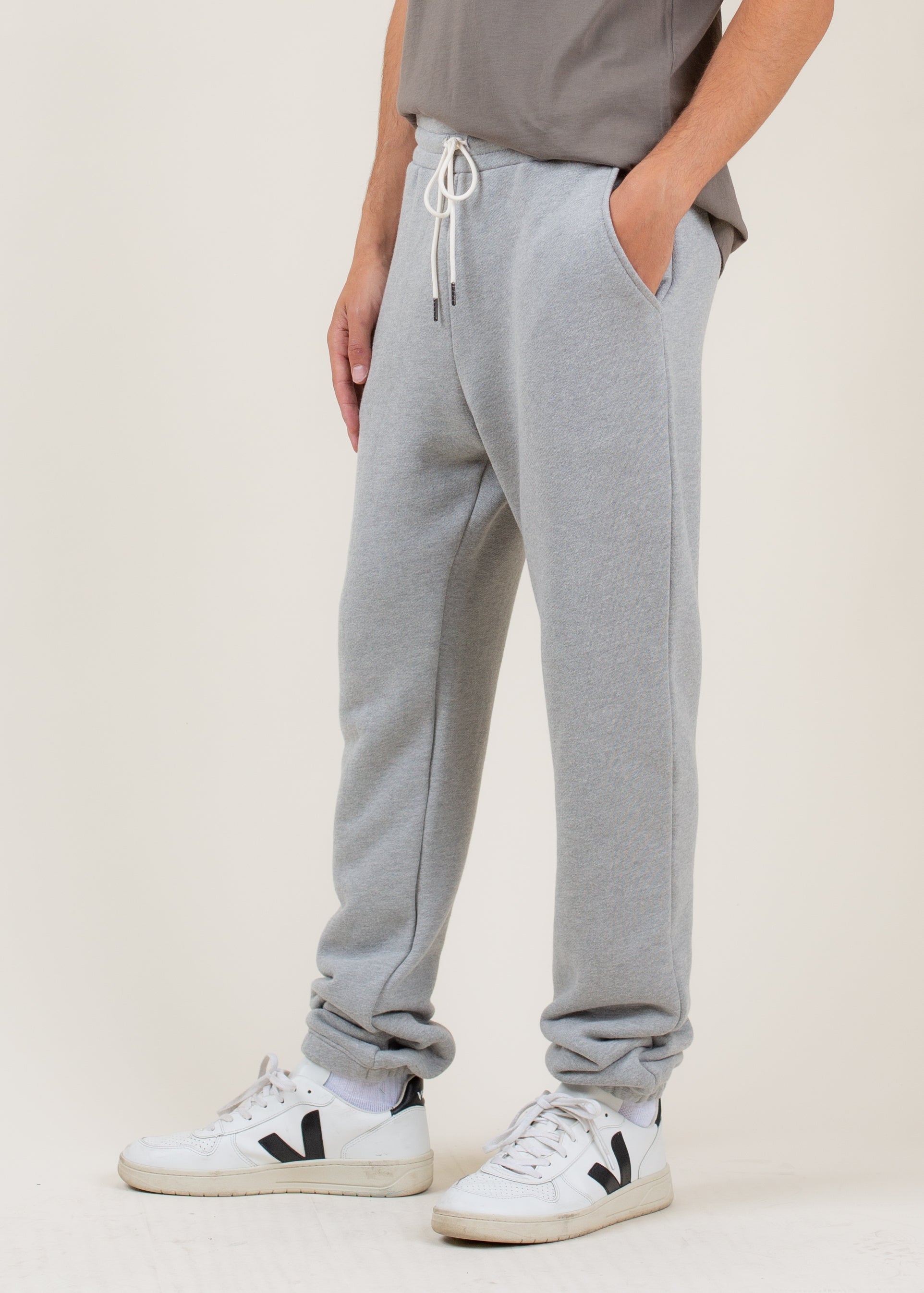 Person wearing gray sweatpants and white sneakers on a plain background