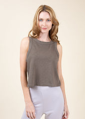 Woman wearing a brown sleeveless top and light gray pants on a beige background