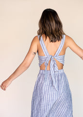 Woman wearing a blue and white striped dress with a tie-back detail on a beige background