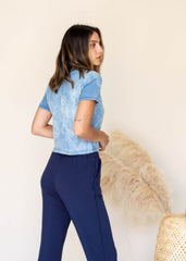 Woman wearing a blue lace top and navy pants against a beige background