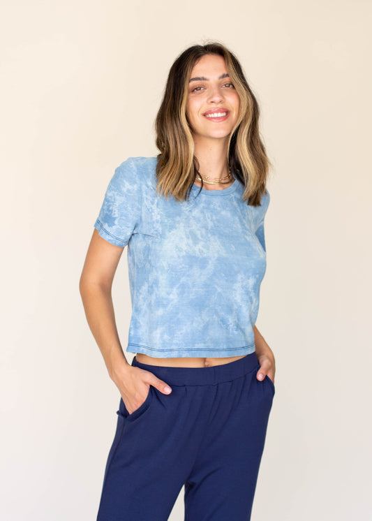 Woman wearing a blue tie-dye crop top and navy pants on a beige background