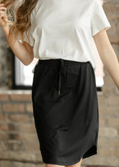 Person wearing a white top and black skirt against a brick wall.