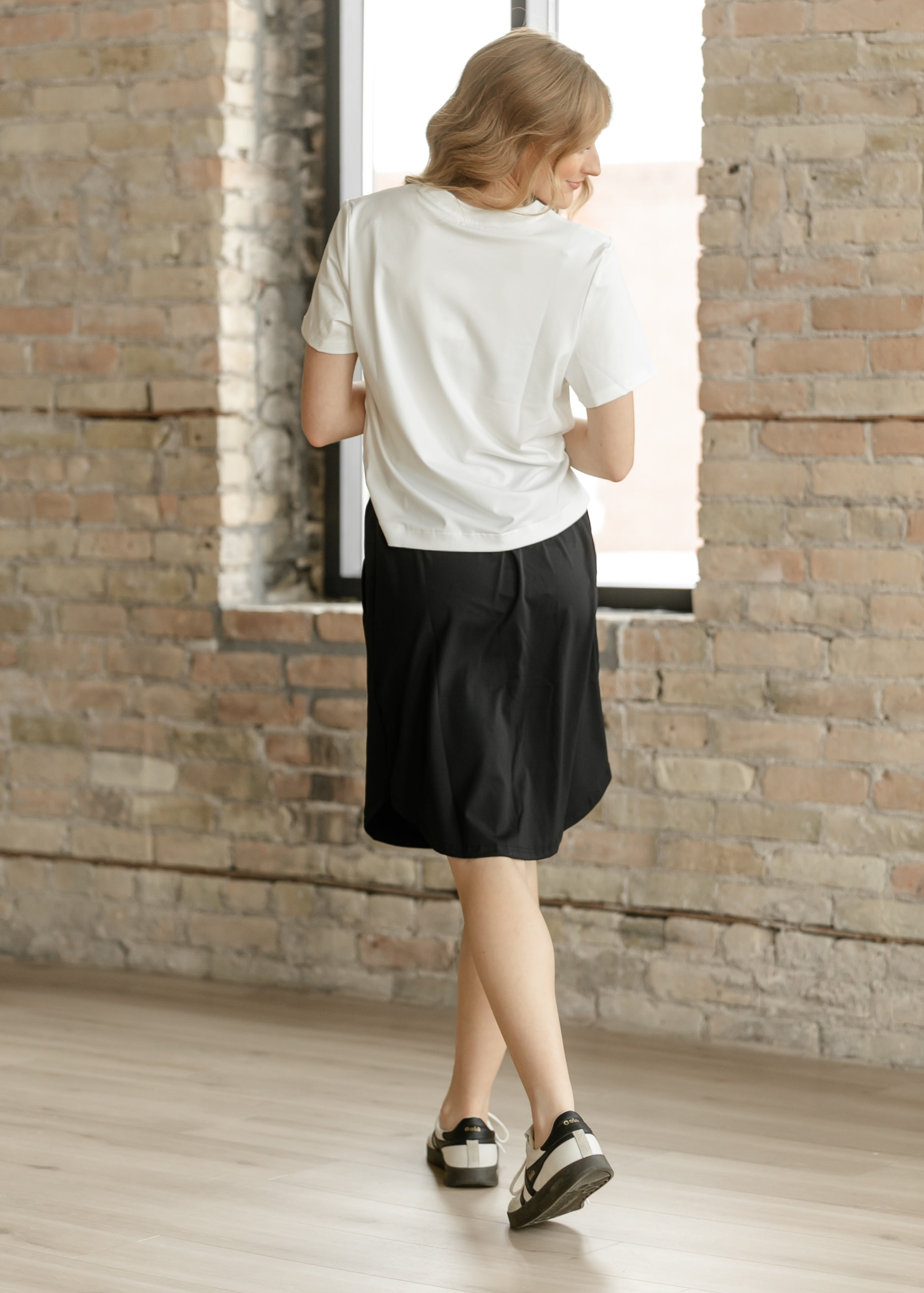 Person wearing a white t-shirt and black shorts standing in a room with brick walls.