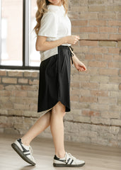 Woman wearing a white shirt and black skirt standing against a brick wall.