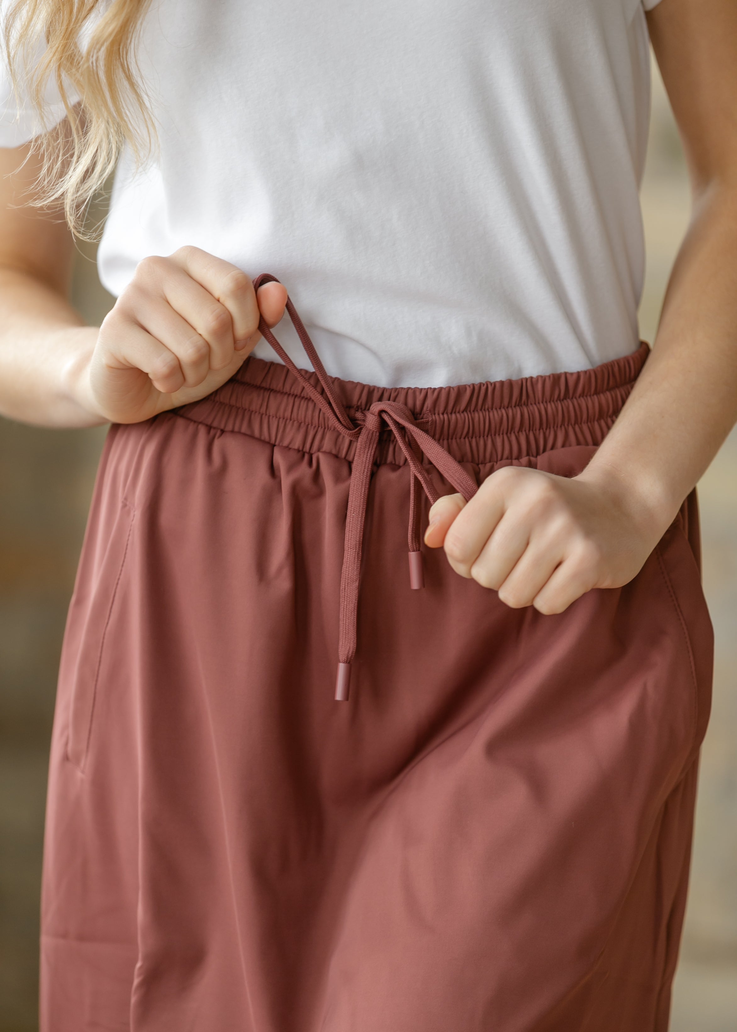 Person wearing a white t-shirt and brown pants with a blurred background