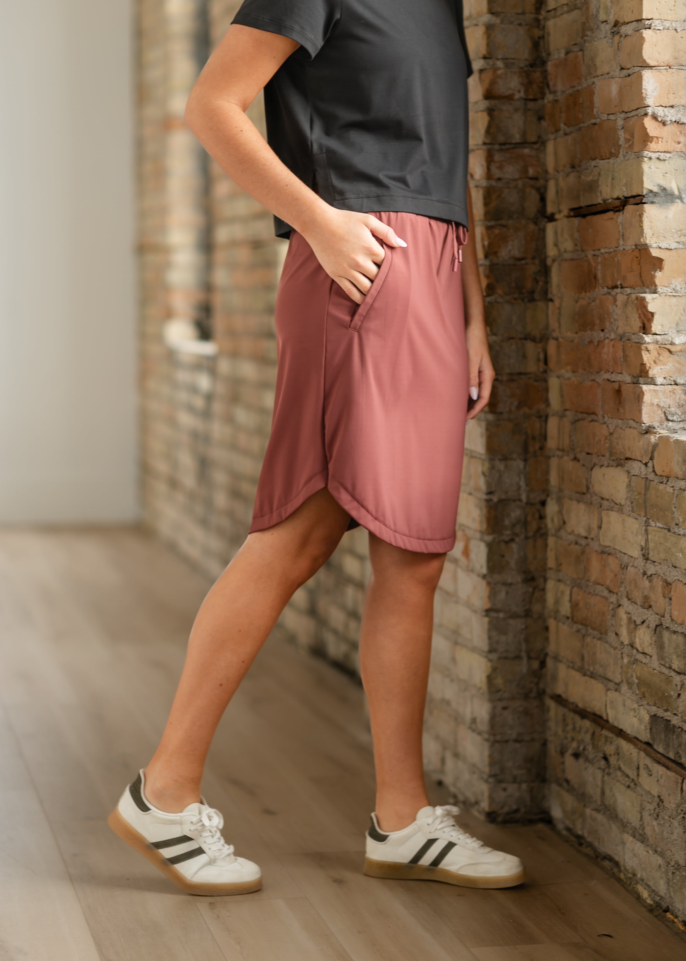 Person wearing pink shorts and black shirt against a brick wall.