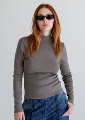 Person wearing a gray long-sleeve top and blue jeans against a plain background