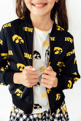 Person wearing a black jacket with yellow 'Iowa' pattern, white shirt, and plaid pants on a white background