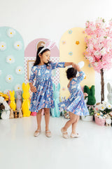 Two children in matching blue floral dresses dancing in a decorated room with Easter decorations.