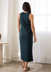 Woman wearing a dark green sleeveless dress standing in a room with white curtains.