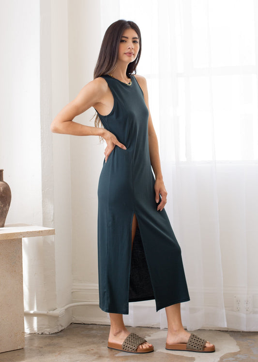 Woman wearing a dark green sleeveless dress with a slit, standing indoors.