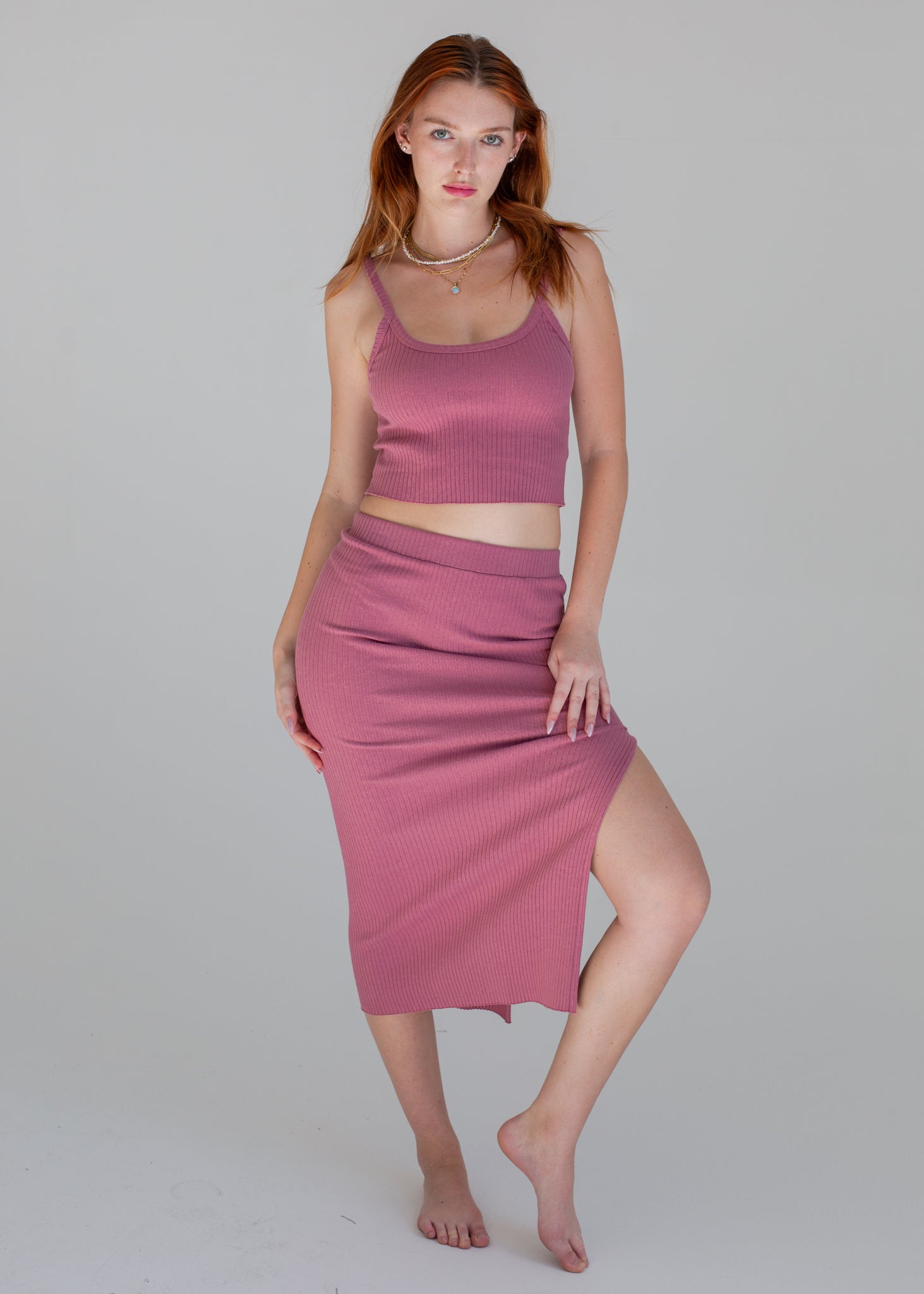 Woman wearing a pink ribbed tank top and skirt on a gray background