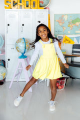 Young girl in a yellow dress standing in a classroom with educational decor.