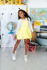 Young girl in a yellow dress standing in a classroom setting with educational decor.