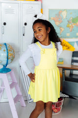 Young girl in a yellow dress standing in a classroom setting with educational items around.