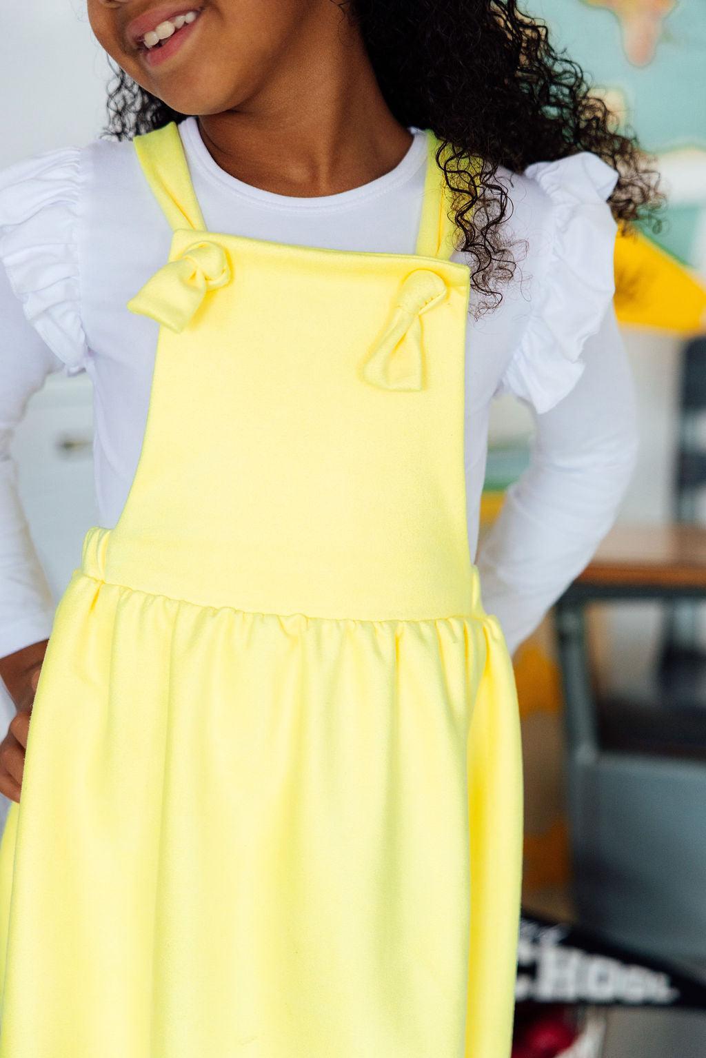 Child wearing a yellow dress over a white shirt with ruffled sleeves.