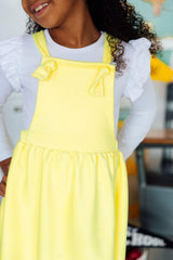 Child wearing a yellow dress over a white shirt with ruffled sleeves.