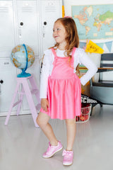 Young girl in a pink dress standing in a classroom setting with educational items around.