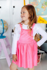 Young girl in a pink dress standing in a room with educational posters and globes.