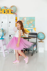 Young girl in a pink tutu standing in a classroom setting with educational decor.