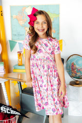 Young girl in a floral dress standing in a classroom setting with educational decor.