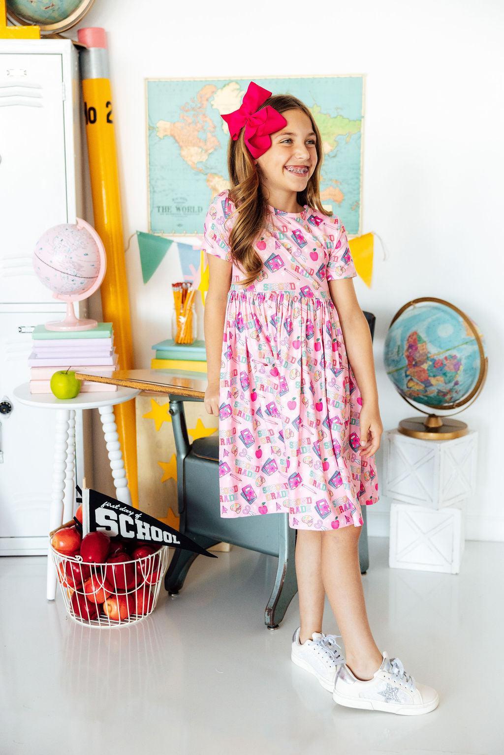 Young girl in a floral dress standing in a classroom setting with educational decor.