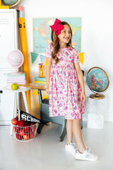 Young girl in a floral dress standing in a classroom setting with educational decor.