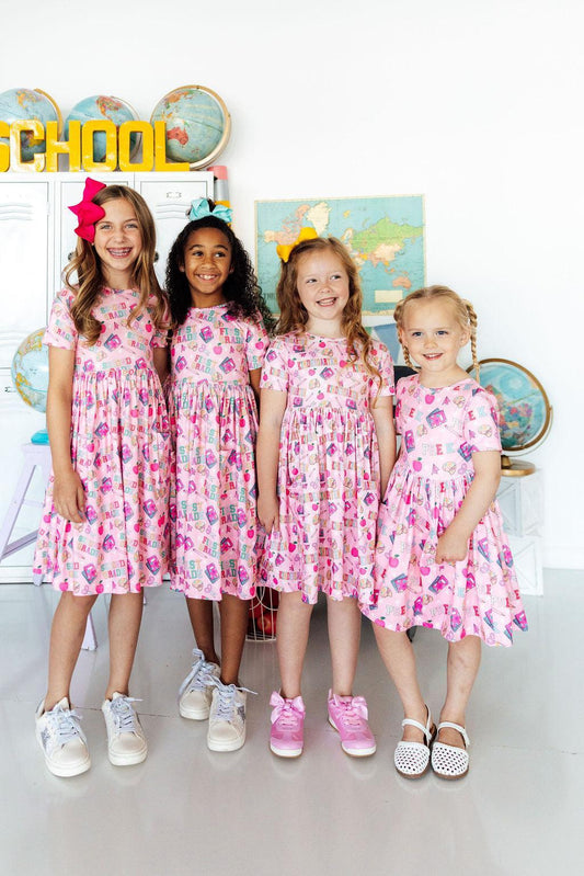 Four young girls in matching pink floral dresses standing in front of a 'Back to School' sign.